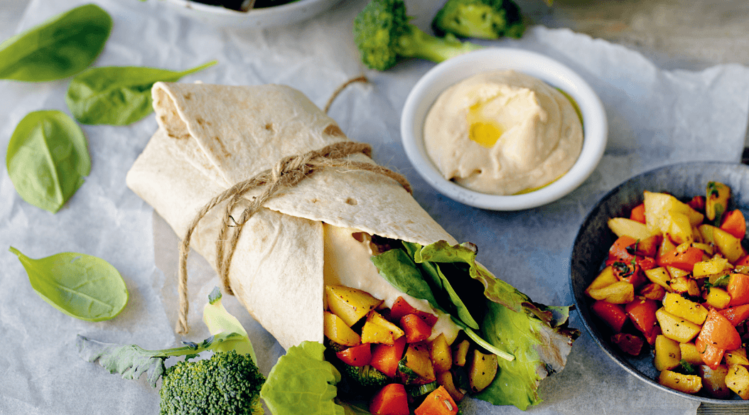 A healthy wrap tied with twine, filled with leafy greens and colorful grilled vegetables, accompanied by hummus and a side of diced seasoned vegetables. Recipes